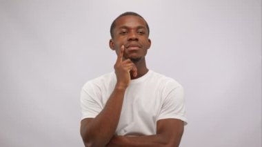 Money rain from dollars suddenly falls on thinkful african american man on white background. Lucky man clenches his fists with joy and looking at camera. Enrichment, winning, easy earnings concept.