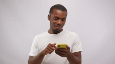 Excited overjoyed african american man browsing smartphone and receiving good news on white background. Feeling euphoric, shouting laughing gambling victory making hand winner gesture clenching fist.