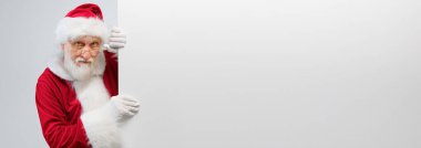 Handsome Santa Claus in glasses and white gloves is holding a large blank board and looking at the camera. Big white banner with Santa Claus