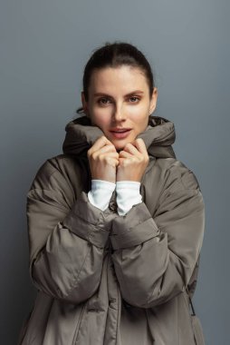 Güz ve kış boyunca gri ceket giyen neşeli, genç bir kadın. Gri stüdyo arka planında soyutlanmış.