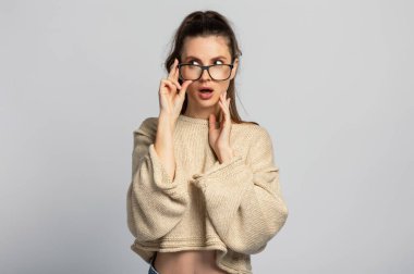 Gözlüklü, güzel ve komik esmer kız etrafa bakıyor. İzole, açık gri arkaplan.