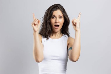 Güzel mutlu esmer kadın, gri arka planda izole edilmiş bir fotokopi alanını işaret ediyor.