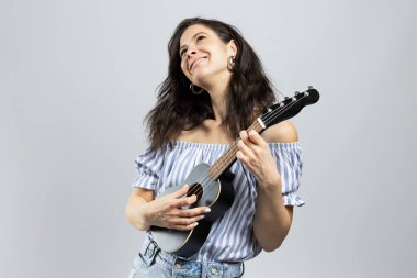 Ukulele çalan çekici esmer kadın, gri arka planda soyutlanmış.