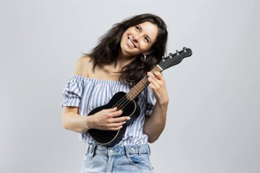 Ukulele çalan çekici esmer kadın, gri arka planda soyutlanmış.