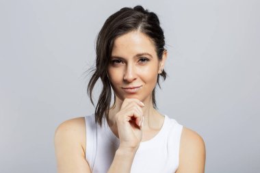 Gri arka planda izole bir şekilde kameraya bakan güzel bir genç kadın.