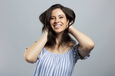 Gri arka planda izole edilmiş kameraya bakan güzel ve neşeli genç bir kadın.