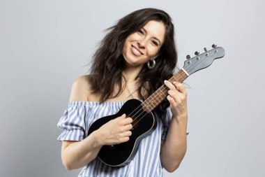 Ukulele çalan çekici esmer kadın, gri arka planda soyutlanmış.