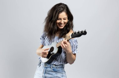 Ukulele çalan çekici esmer kadın, gri arka planda soyutlanmış.