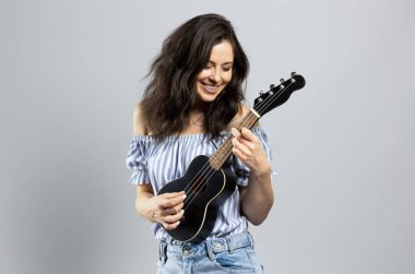 Ukulele çalan çekici esmer kadın, gri arka planda soyutlanmış.