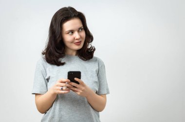 Neşeli, güzel, genç bir kız elinde bir cep telefonu tutuyor ve başka yere bakıyor, kopyalama alanı, gri arka planda izole edilmiş.
