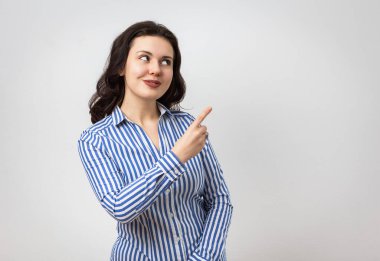 Çekici gülümseyen esmer kız gülümseyen yüzüyle yukarı bakıyor, açık gri arka planda duruyor.