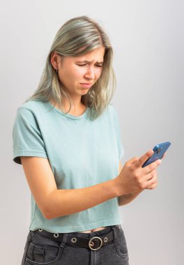 Telefondaki genç kadın iğreniyor. Gri arkaplanda izole.