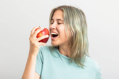 Kırmızı bir elmayı ısırmak üzere olan genç ve tatlı bir kadın. Gri arkaplanda izole
