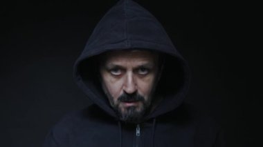 Siyah kapüşonlu bir adam burnundan sigara dumanı üflüyor. Karanlık atmosfer, siyah arkaplan.