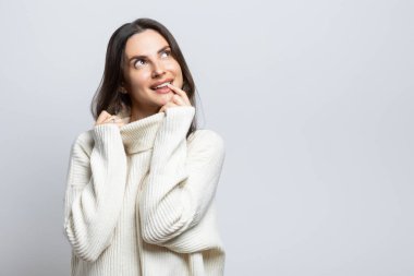 Beyaz bir süveter giyen genç ve güzel bir kadın bir şey tarafından cezbedildi. Beyaz arkaplanda.