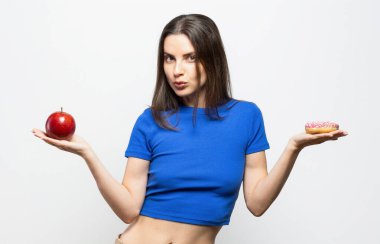 Donut ve kırmızı elma arasında seçim yapmak zorunda kalan güzel bir genç kadın. Beyaz arkaplanda