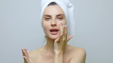 Güzel genç bir kadın aynanın önünde cildine bakıyor, yüzünü kontrol ediyor. Güzellik, cilt bakımı. Beyaz arkaplanda