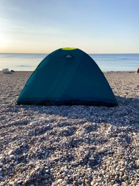 Deniz sahilinde kamp yapan aile, arka planda dağlar, deniz kenarında kamp çadırı, bağımsız turizm konsepti.