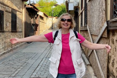 Antalya 'nın eski caddesinde sırt çantalı, güneş gözlüklü orta yaşlı bir kadın. Yaz aktif turizm konsepti. Açık havada.