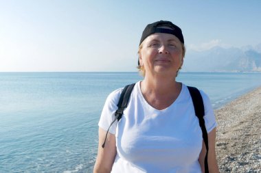 Deniz sahilinde sırt çantalı, maceraperest bir kadın. Emekliler için yaz turizmi. Açık havada.