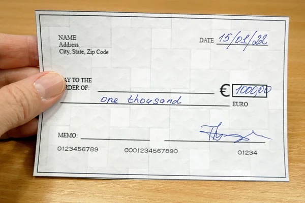 Hand holds a bank check on wooden table background, Blank bank cheque, Prepare writing a check, closeup, top view