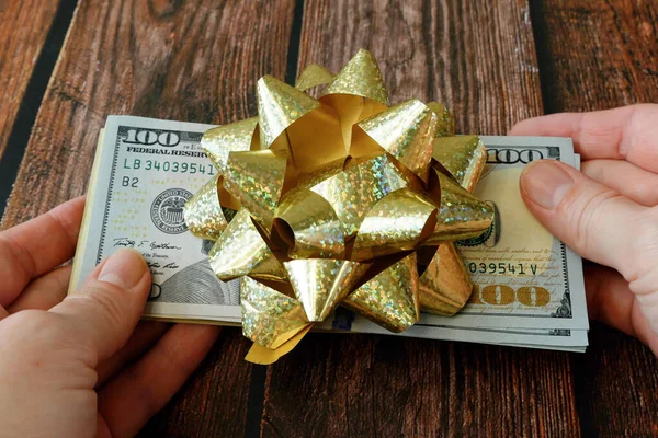 Money gift, big stack of money with golden bow on wooden background, concept