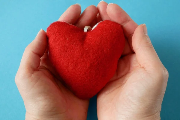 Red heart symbol in hand on blue background. american heart month in February, closeup
