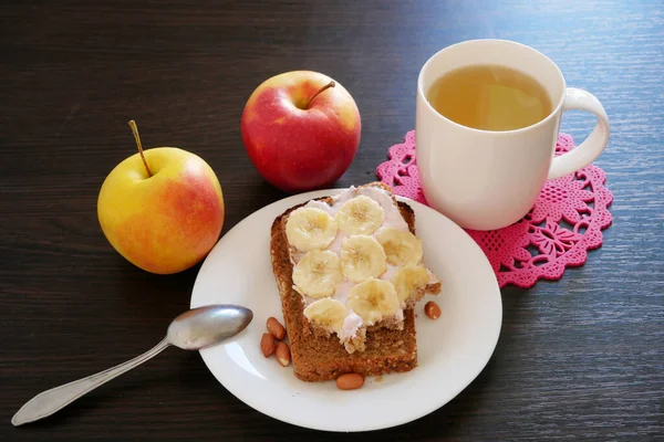 三明治 配上麦片面包 淡牛奶奶油和香蕉 木桌上的热绿茶 特写镜头 — 图库照片
