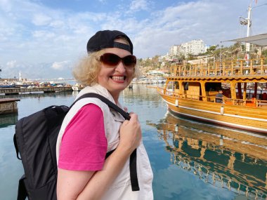 Sırt çantalı orta yaşlı kadın eski Antalya Türkiye şehrinde gemi, yat ve teknelerin yanında kalıyor. Emekliler için yaz turizmi. Macera yaşsızdır, açık havada.