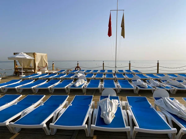 Deniz suyunun yanında boş plaj sandalyeleri ve şemsiyeler. Terk edilmiş yaz tatil köyünün manzarası. Kumsal sandalyeleri ya da kumlu deniz kıyısındaki güneşli şemsiyeler. Açık havada.