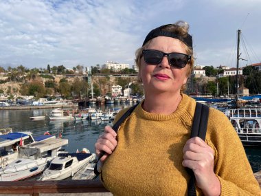 Antalya Türkiye 'nin eski kentinde marinada gemi, yat ve teknelerin yanında kalan sırt çantalı yaşlı kadın. Emekliler için yaz turizmi. Macera yaşsızdır, açık havada.