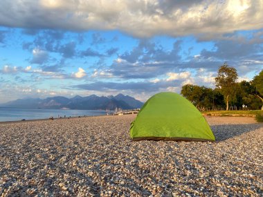 Deniz sahilinde kamp yapan aile ve arka planda dağlar, deniz veya okyanus sahilinde kamp çadırı, bağımsız turizm konsepti.