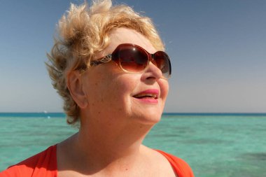 Alnındaki teri deniz sahilinde havluyla silen son sınıf öğrencisi bir kadın. Dışarısı ve dışarısı için anormal derecede sıcak.