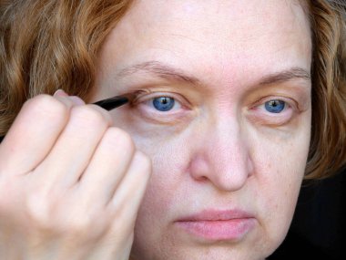 Makyaj yaparken göz kapağı sarkık orta yaşlı bir kadın gözü. Ptosis, göz kapağının üst kısmının sarkmasıdır, tembel göz. Kozmetik ve yüz konsepti, ilk kırışıklıklar, yakın çekim.