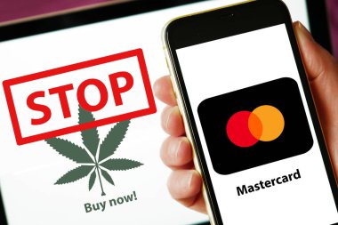 Lviv, Ukrayna - 27 07 2023: ekranda Mastercard logosu olan akıllı telefon ve arka planda esrar yaprağı ve kelime durdurma ile dizüstü bilgisayar. ConceptConceptConcepMastercard, kartlarıyla esrar satın alınmasını yasaklıyor. Kavram