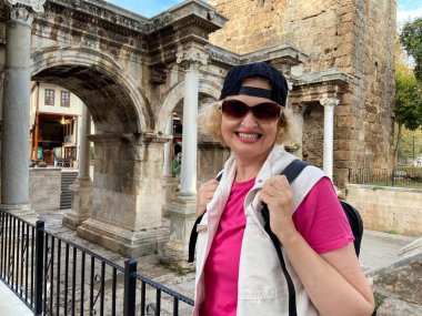 Sırt çantalı orta yaşlı kadın eski Antalya Türkiye şehrinde gemi, yat ve teknelerin yanında kalıyor. Emekliler için yaz turizmi. Macera ölümsüzdür.