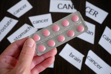 Bir el, arka plandaki yırtık kağıt parçalarının üzerinde kanser, diyabet, hipertansiyon gibi çeşitli hastalıkların teşhislerini içeren hapları tutar. Hastalıkların başarılı tedavisi, konsept