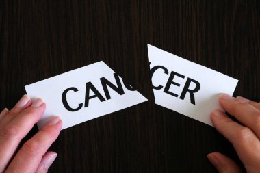 Siyah ahşap zemin, başarılı tedavi stratejisi ve konsept üzerine CANCER yazılı iki kağıt parçasını el ele tutuşmak