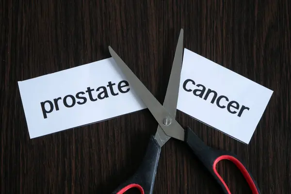 The scissors cutting paper with text prostate CANCER on black wooden background, successful treatment strategy, concept
