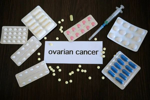 Hand holding the inscription ovarian CANCER on the paper on many pills and drugs background, closeup, concept