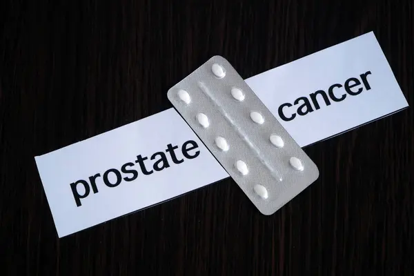 Pills in blister between the two pieces of paper with text prostate CANCER on black wooden background, successful treatment strategy, concept