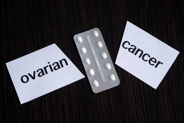 Pills in blister between the two pieces of paper with text ovarian CANCER on black wooden background, successful treatment strategy, concept