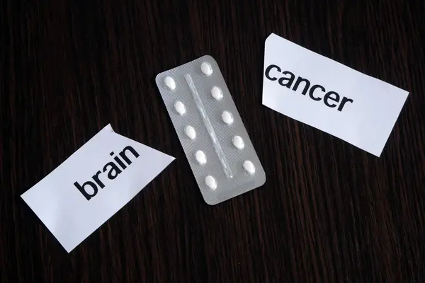 Pills in blister between the two pieces of paper with text brain CANCER on black wooden background, successful treatment strategy, concept