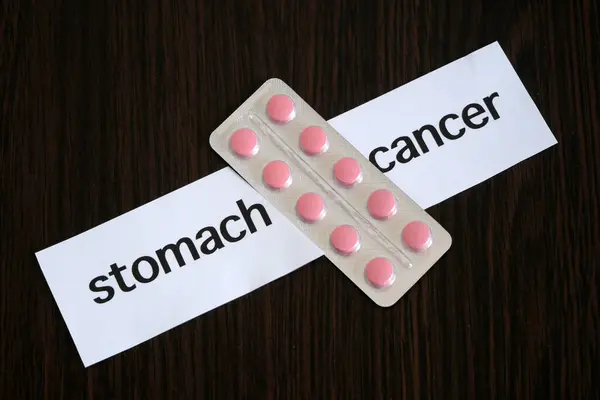Pills in blister between the two pieces of paper with text stomach CANCER on black wooden background, successful treatment strategy, concept