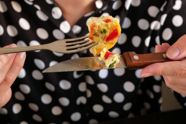 Kadın eli omleti domates, sebze, peynir, çatal ve bıçakla tutuyor. Lezzetli bir kahvaltı, yakın plan.