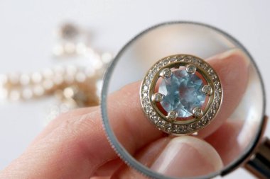 Mavi taşlı klasik altın küpe, büyüteçle mücevhere bakan kuyumcu, mücevher dükkanının konseptini inceler ve onaylar.