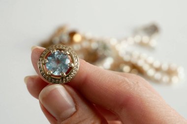 Mavi taşlı klasik altın küpe, büyüteçle mücevhere bakan kuyumcu, mücevher dükkanının konseptini inceler ve onaylar.