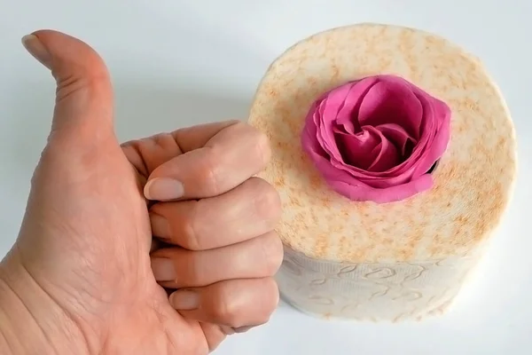 thumbs up on the background of a roll of toilet paper and a rose bud, gentle and soft toilet paper with rose fragrance