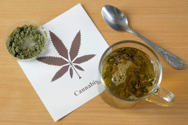 Cannabis herbal tea and marijuana leaves on wooden desk, glass of hemp tea with hemp leaves, top view