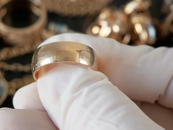 Pawnshop worker verify golden wedding ring  on many golden and silver jewelleries and money background. Customers Buy and Sell Precious Metals, Jewels, Ancient Coins and Second Hand Appliances. Closeup
